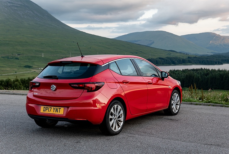 Red car facing green hills and a lake